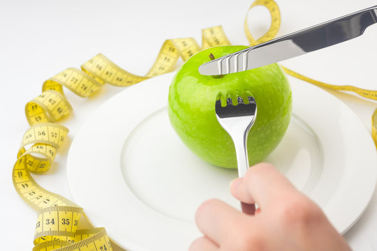 Diet concept, green apple on a white plate, yellow measuring tape, fork, knife, woman cuts fruit, weight loss, healthy diet