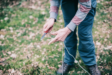 Hands of man cutting rope for preparing campsite.