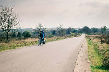 Tourist with backpack walking with bicycle on road in moorland.