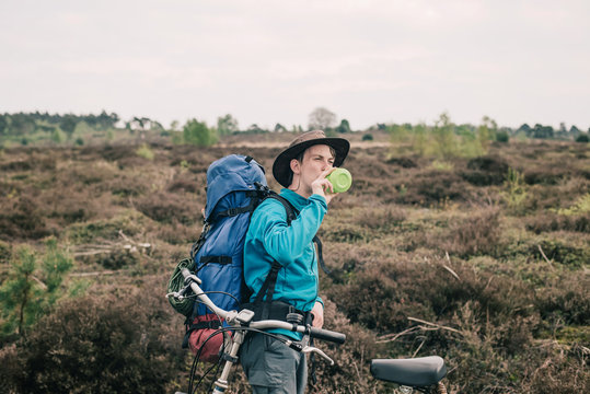 Nomad standing next to bicycle in moorland drinking from bottle.