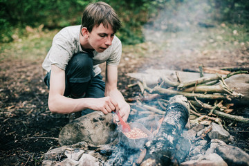 Obraz premium Wayfarer stirring meal in frying pan on campfire.
