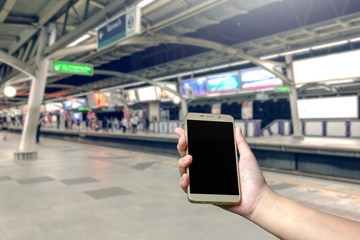 Close up on hand holding cell phone with blank screen for your advertising or promotional content, at train station and blur background. It's dicut object on screen with paths file.