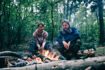 Obraz premium Two men sitting around campfire in spring forest.