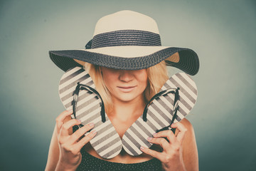 Woman wearing sun hat, holding flip flops