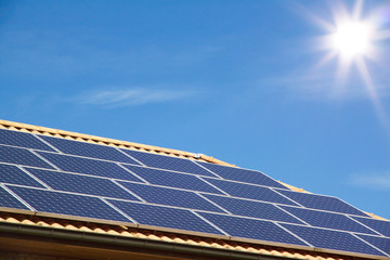 Photovoltaics on the roof of a residential building for alternative energy production in front of blue sky with sunshine and copyspace