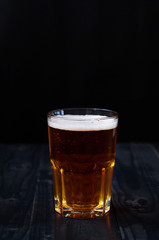 Just a glass of beer on a dark background. A glass of light beer on a wooden table.