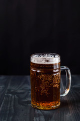 Just a glass of beer on a dark background. A glass of light beer on a wooden table.