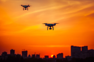 Two modern Remote Control Air Drones Fly with action cameras in dramatic orange sunset sky. Cityscape silhouette in the background. Modern technologies. Kiev, Ukraine. Travel, hobby, inspiration