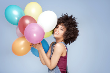 Fototapeta na wymiar Happy young girl with afro holding balloons.