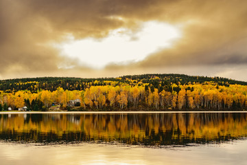 Autumn landscape with foliage colors reflecting on a lake.  Cloudy sky.