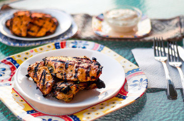 Grilled chicken on a plate with sweet potatoes and sauce in the background. These lean chicken breasts were marinated and cooked on the bbq (Barbecue). The perfect food for a healthy summer meal!