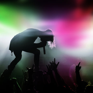 Metal singer and fans silhouette in a music concert with colorful light green and pink.