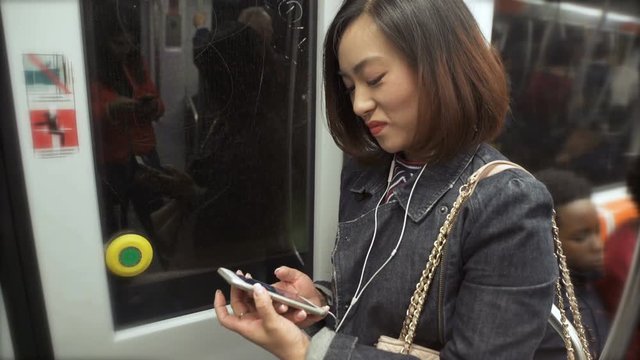 Young Chinese woman on the subway focused on writing on the smartphone