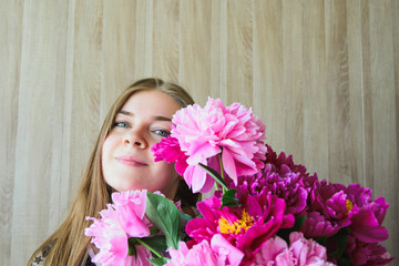 Portrait of a young beautiful blonde caucasian young woman keeps bouquet pink and red peonies flowers