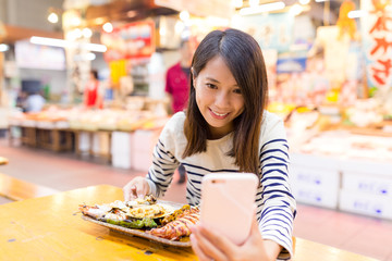 Woman taking selfie by mobile phone with seafood in wet market