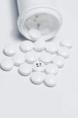 White pills spilling out of a plastic medicine bottle, one with negative emotion