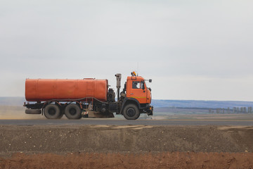 A red watering truck at highway among field - construction work