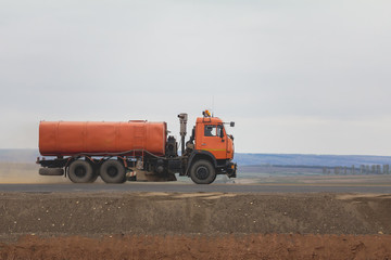 Obraz premium A red watering truck at highway among field - construction work
