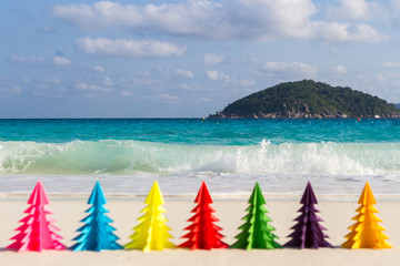 Seven paper Christmas trees stand in the sand against the blue sea. Similan Islands