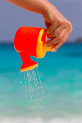 Female hand pours water from a children's plastic watering can. Andaman sea, Similan Islands