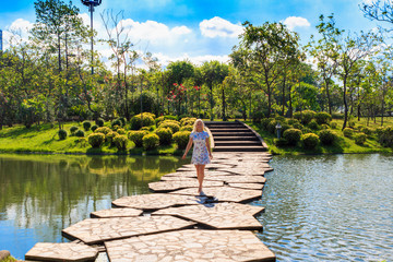 A beautiful woman stands on an artificial path through the river in the Park. Sunny day.