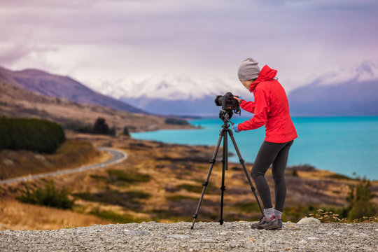 Photographer taking New Zealand travel nature photography. Woman photographer with slr camera on tripod at sunset with beautiful landscape in background. Peter's lookout, famous tourist destination.