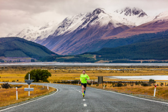 Running runner man running on road in mountain landscape in New Zealand travel destination. Male athlete runner training cardio on cold sunrise morning exercising alone on nature background.
