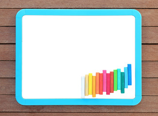 Blank white blackboard with colorful chalk on wooden plank.