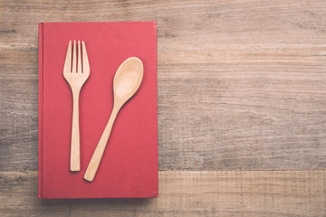 Top view spoon, fork and book on wooden plank background