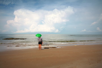 Obraz premium Woman standing holding a green umbrella on the beach