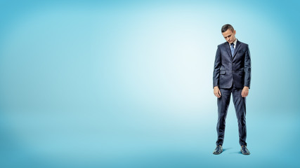 A depressed businessman standing with shoulders slumped on blue background.