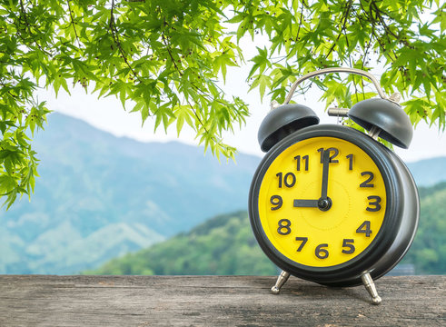 Closeup black and yellow alarm clock for decorate in 9 o'clock on blurred leaves and mountain view background