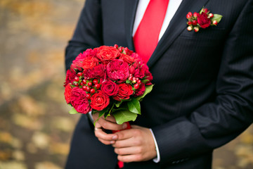 groom holding bridal bouquet close up. red garden roses decorated in composition