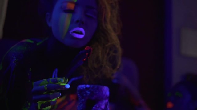 Closeup view of sexy woman filmed in fluorescent clothing under UV black light blowing on live coals from hookah