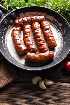 Grilled sausage in a pan and fresh vegetables on wooden table