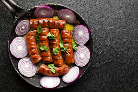 Grilled sausage with onion in a pan on black background