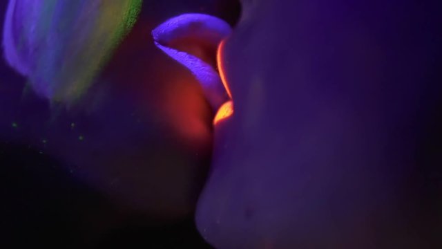 Closeup view of two girls in fluorescent clothing under UV black light kissing. Homosexual relations.