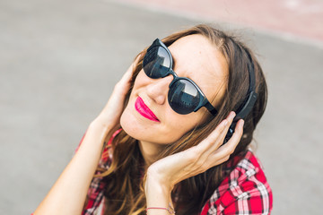Young smiling woman relaxing and listening to music with headphones in the street.