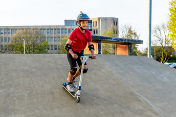 Day view teen boy riding scooter on skating playground