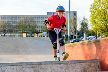 Day view teen boy riding scooter on skating playground