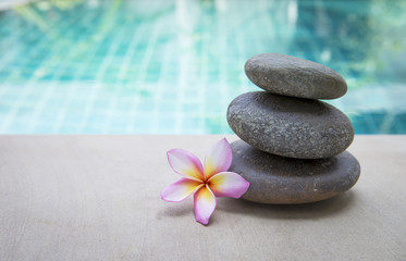 Fototapeta na wymiar Zen spa stone with plumeria flower over blurred blue swimming pool background