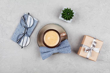 Morning coffee mug, gift, glasses and bowtie on stone table top view in flat lay style for breakfast on Happy Fathers Day.