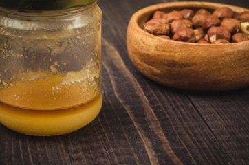 honey and nuts against a dark background/glass jar of honey and wooden plate with nuts