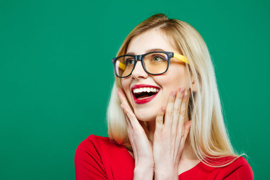 Laughing Girl in Eyeglasses and Red Top on Green Background. Closeup Portrait of Young Blonde with Long Hair and Charming Smile in Studio.