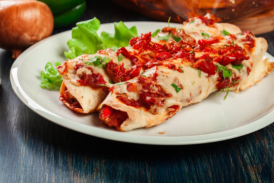 Traditional mexican enchiladas with chicken meat, spicy tomato sauce and cheese on a plate