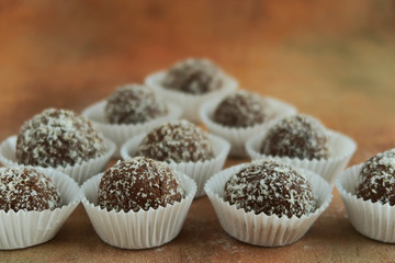 Coconut and chocolate balls in white paper cupcakes  on vintage brown background.