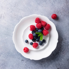 Freshly picked blueberries and raspberries on white plate on gray stone background. Concept for healthy eating and nutrition with copy space. Top view.