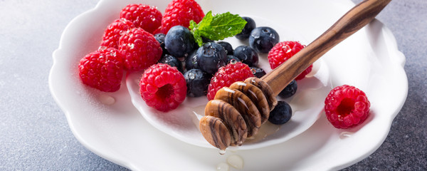 Freshly blueberries and raspberries on white plate with honey. Healthy eating and nutrition concept with copy space.