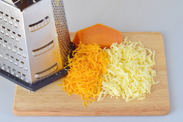 Step by step cooking. Grated gouda and cheddar cheeses with a grater on a wooden cutting board on a gray background