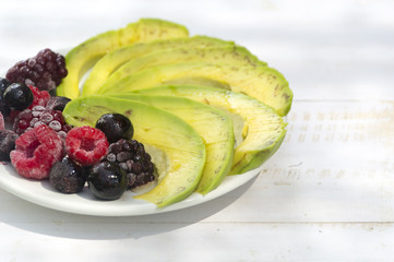 Healthy breakfast ingredients avocado slices with mix berries and honey.